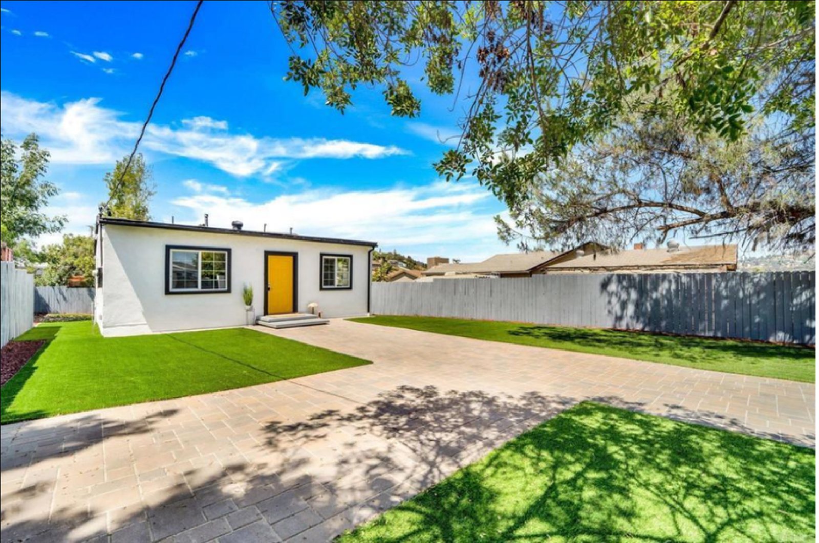A detached single-storey unit with a yellow door in a paved rear yard